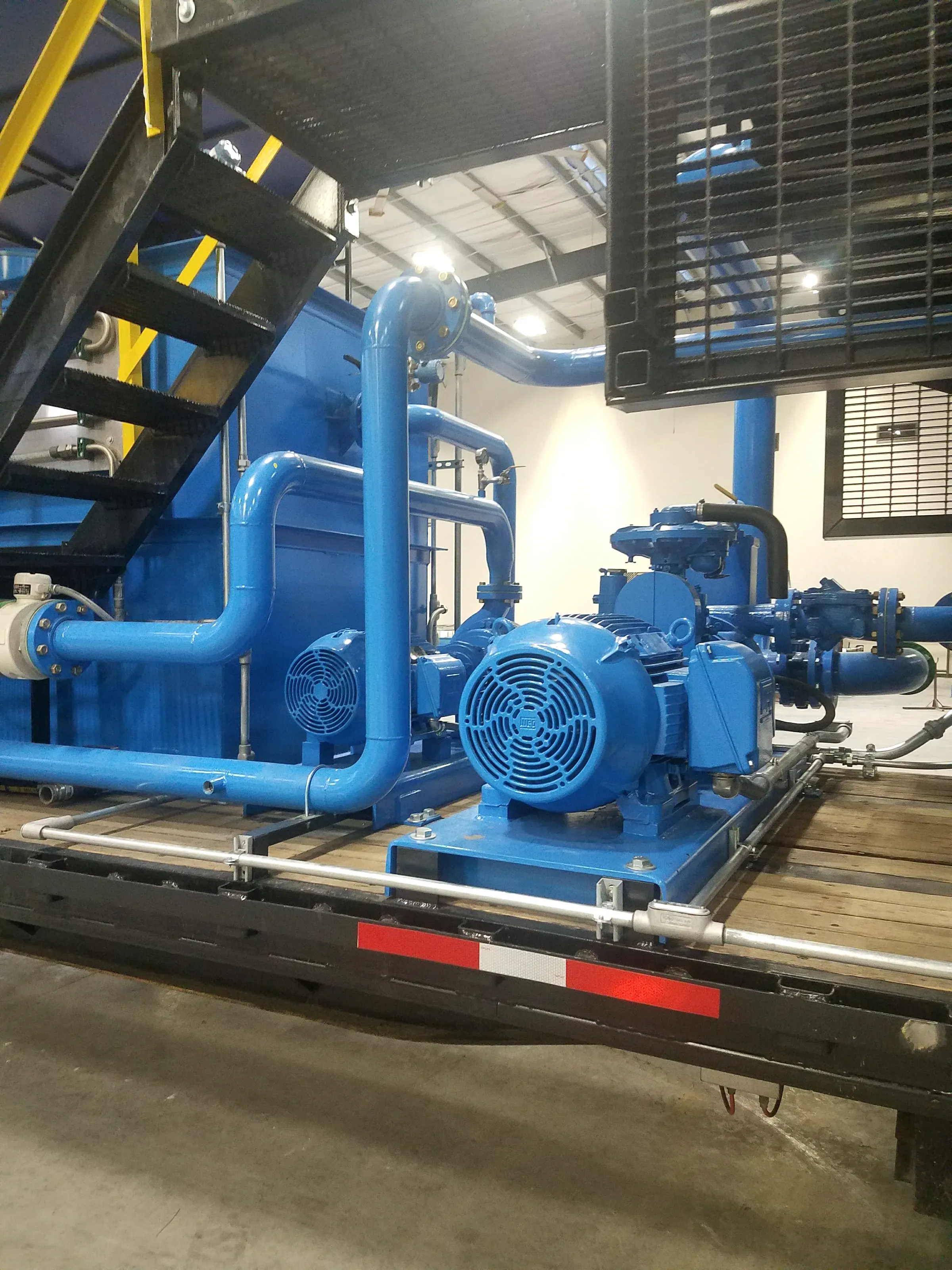 Blue-painted blower and recycle pump skid with looping process piping on a DAF build inside the fabrication shop
