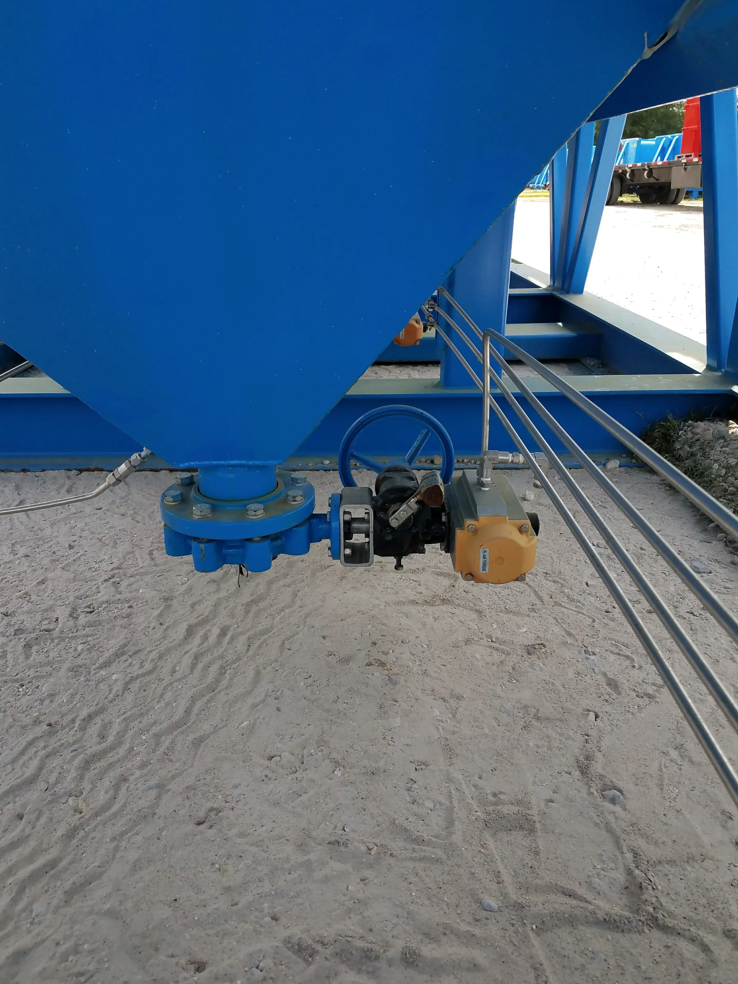 Underside of a blue cone-bottom hopper showing the flanged discharge and actuated butterfly valve