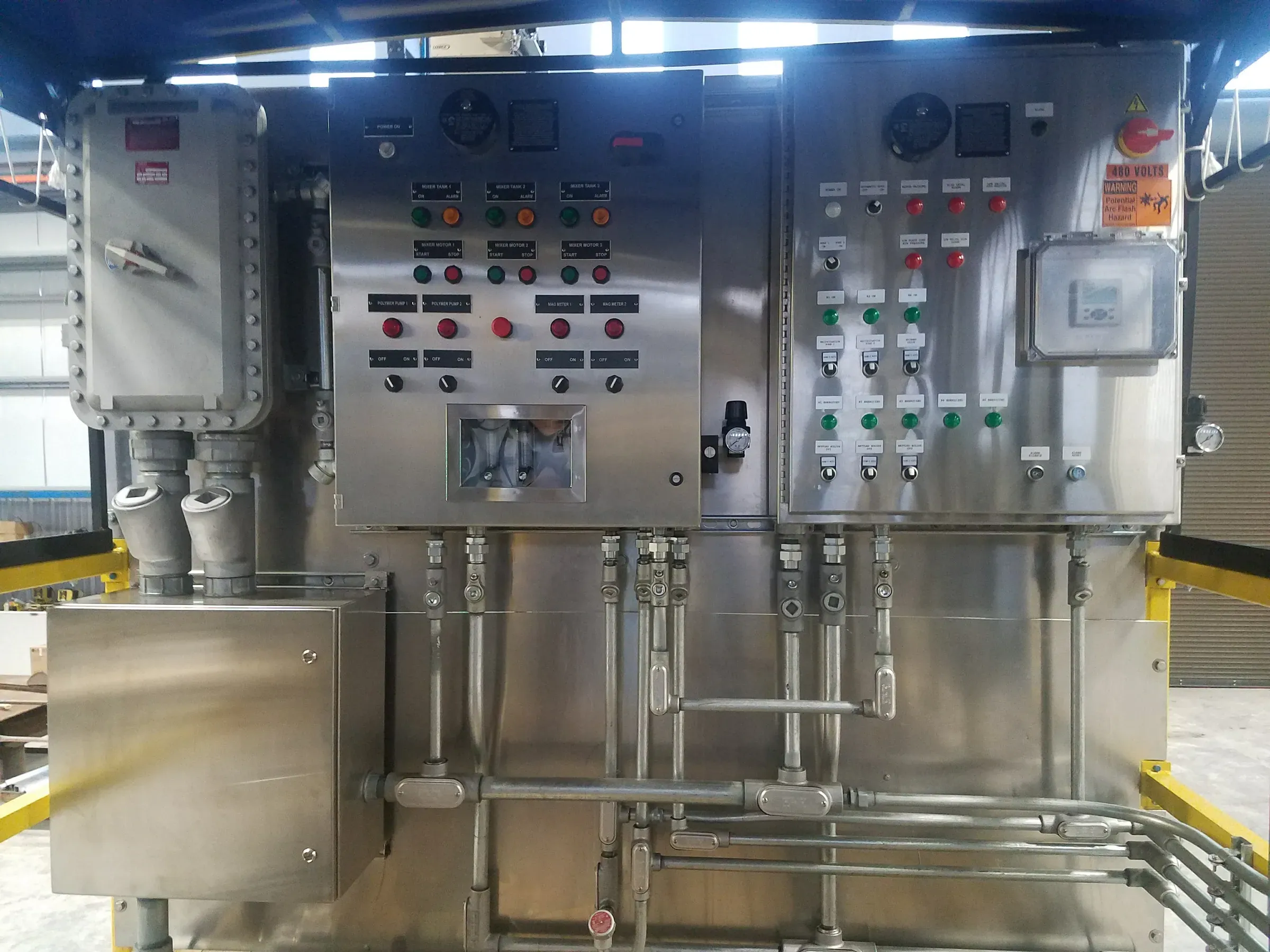 Twin stainless steel control panels with labelled mixer and polymer pump switches, indicator lights and rigid conduit on a treatment skid