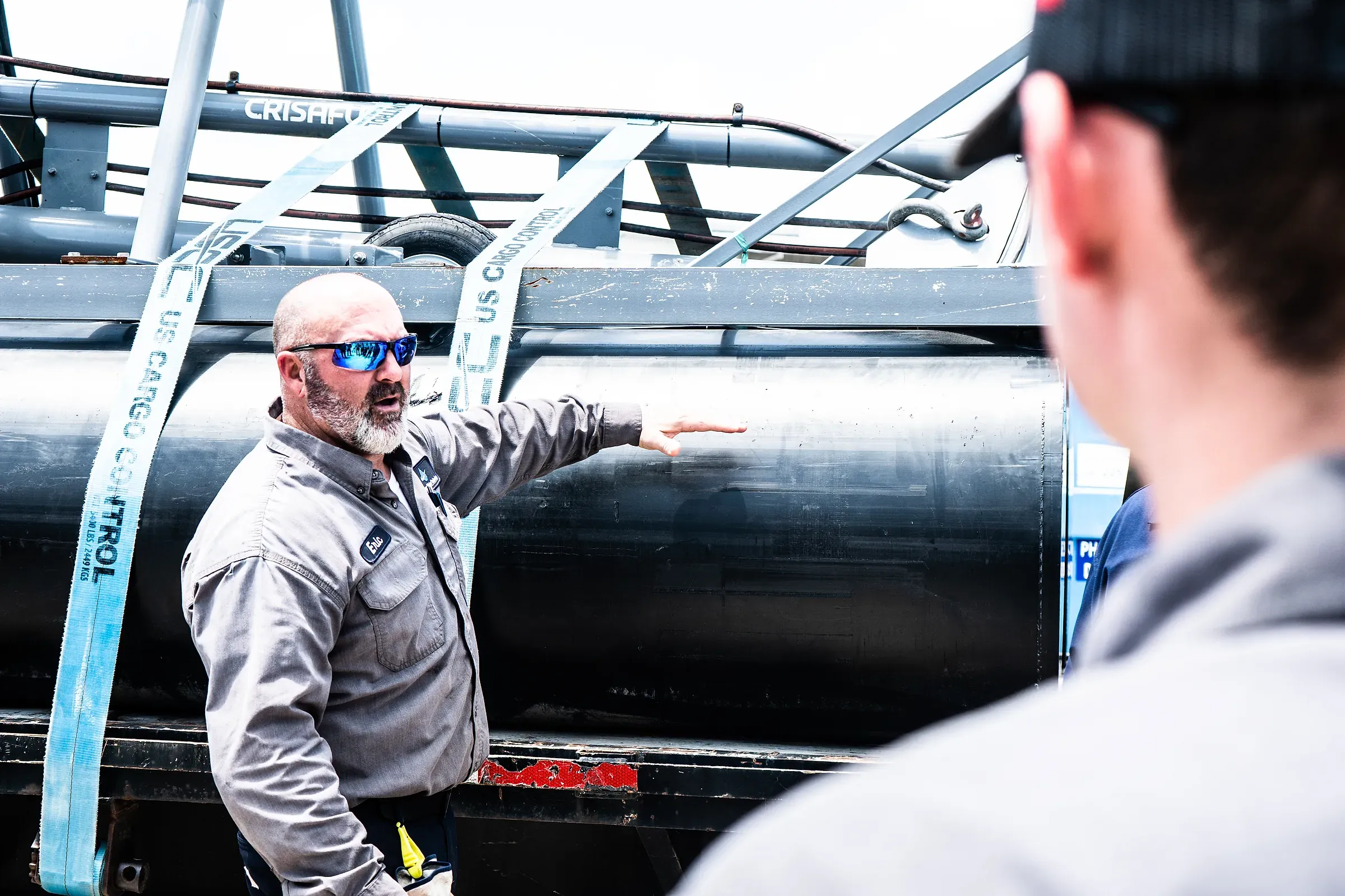 Spectrum supervisor gesturing along a large dredge discharge pipe on a trailer while a colleague listens