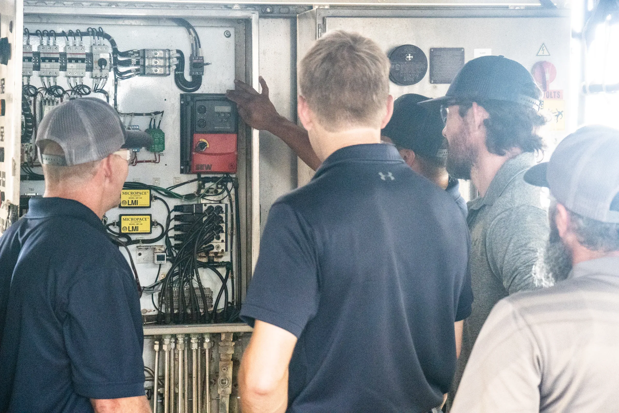 Spectrum crew and plant operators gathered at an open control panel on site, one of them pointing out a variable-frequency drive