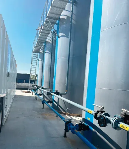 Battery of grey treatment tanks with blue trim and interconnected inlet piping at Spectrum's Lake Charles centralized wastewater treatment facility