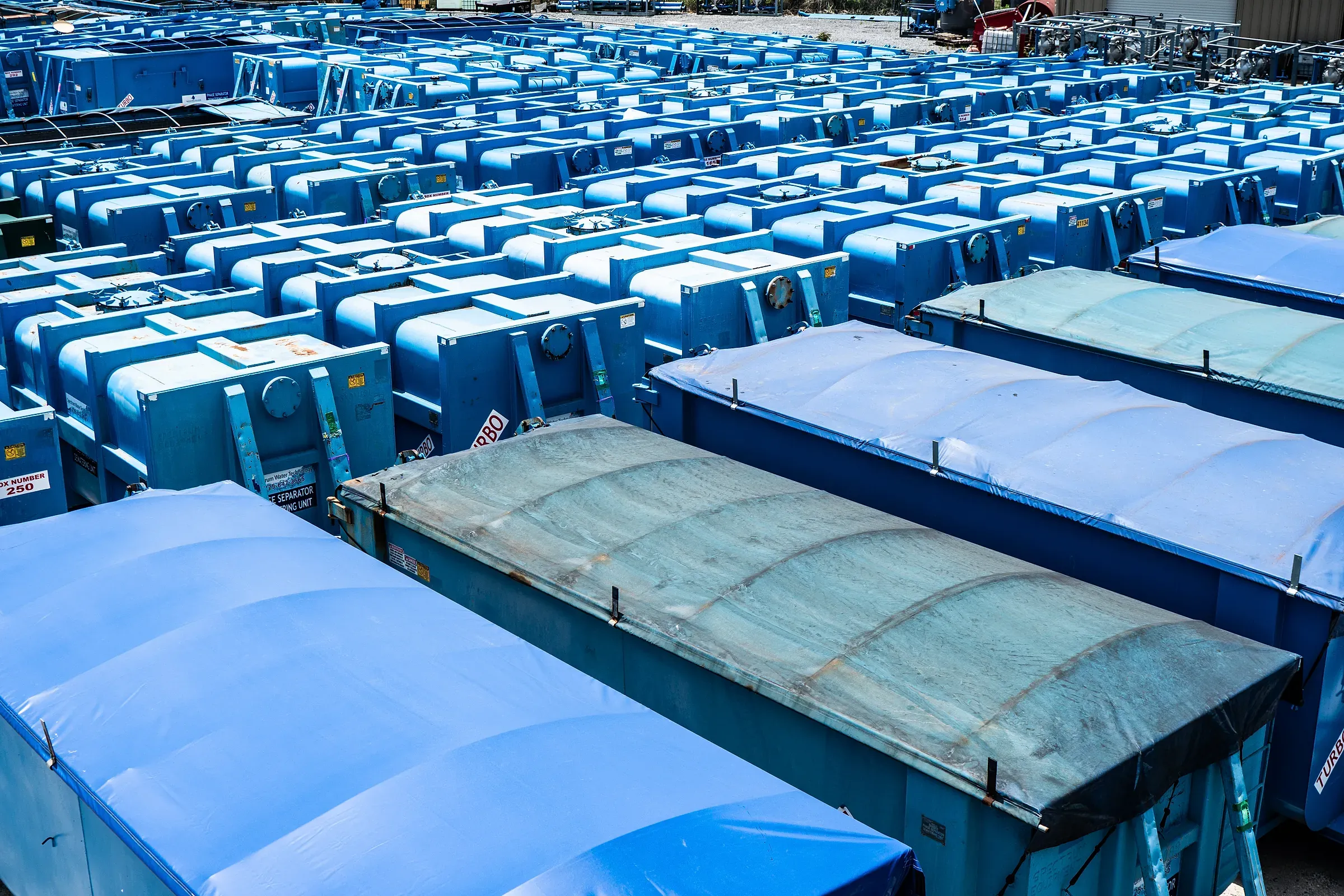 Elevated view across dozens of blue Turbo Phase Separator dewatering boxes ranked in tight rows, tarped units in the foreground