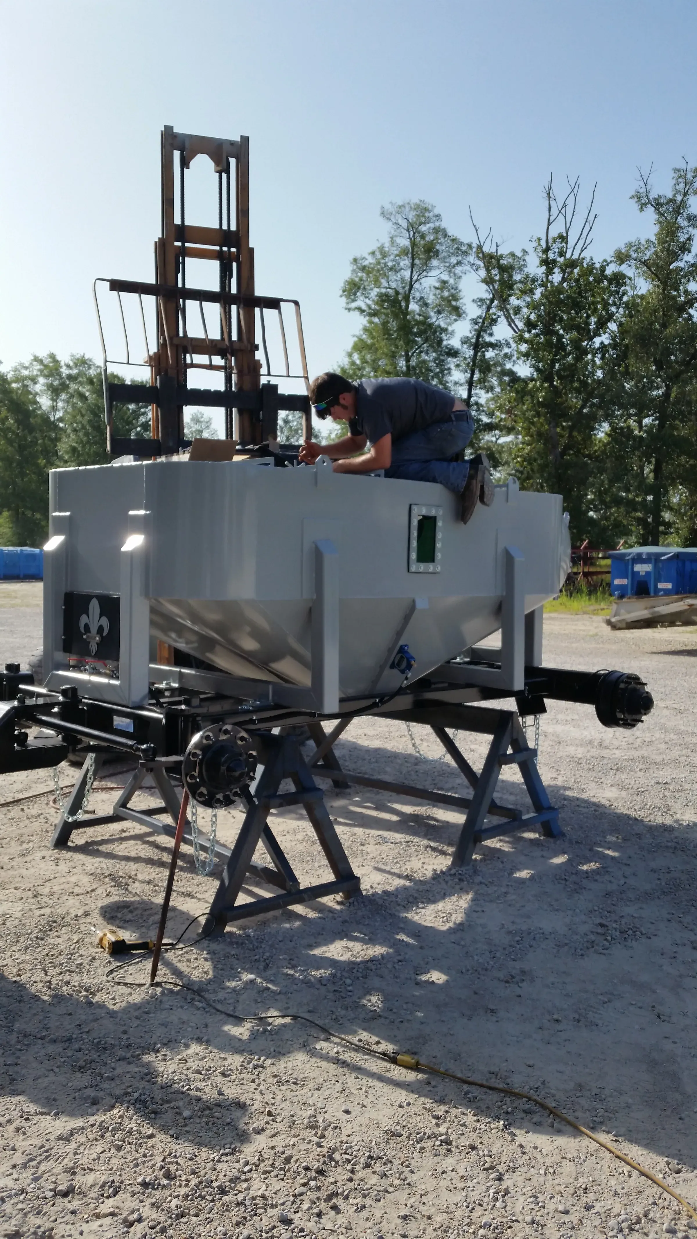 Technician kneeling on top of a newly built white trailer-mounted dewatering unit on stands in the yard, wiring the control panel under a clear sky