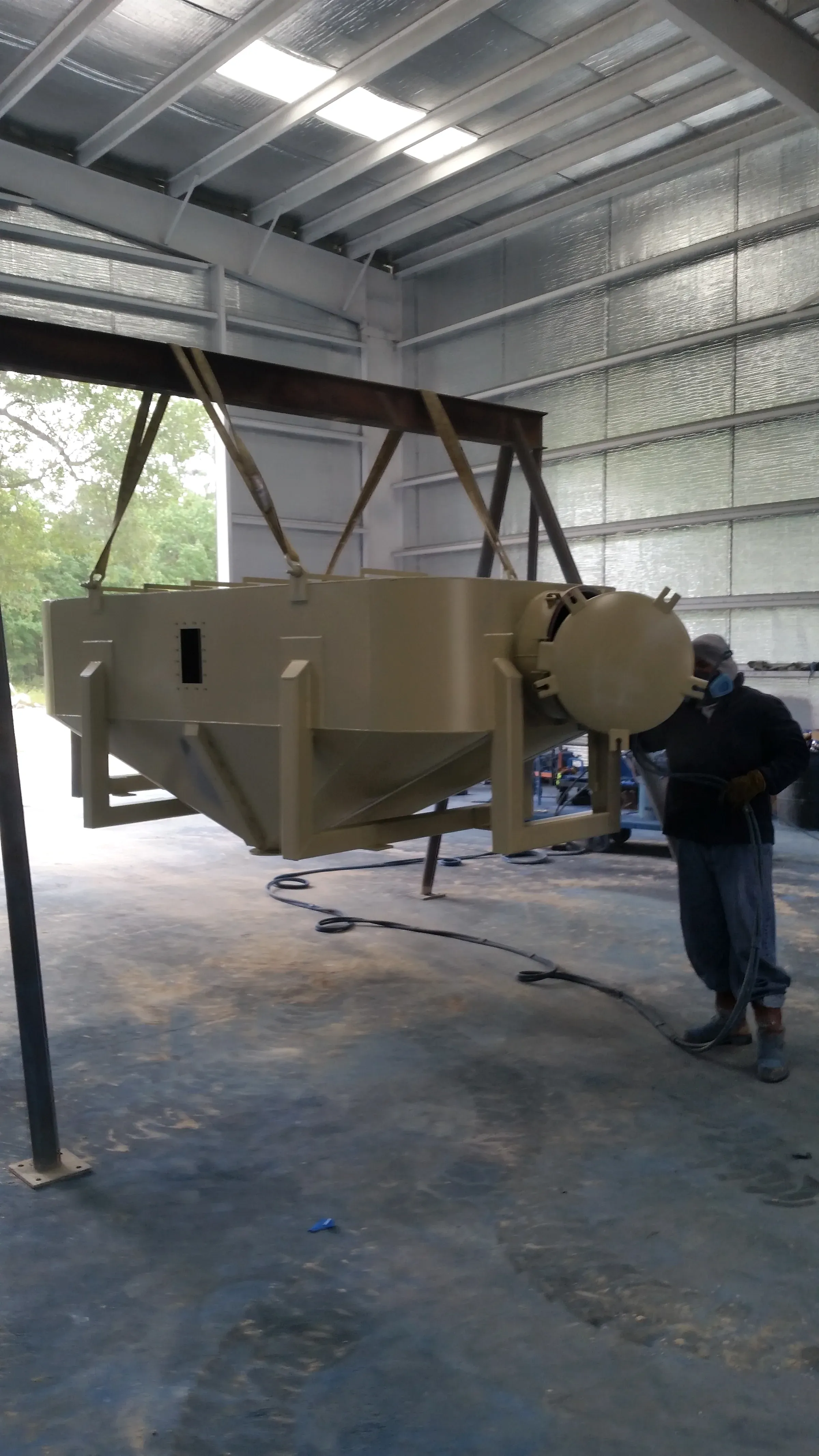 Fabricator in a respirator working on a cone-bottom hopper vessel inside the fabrication shop