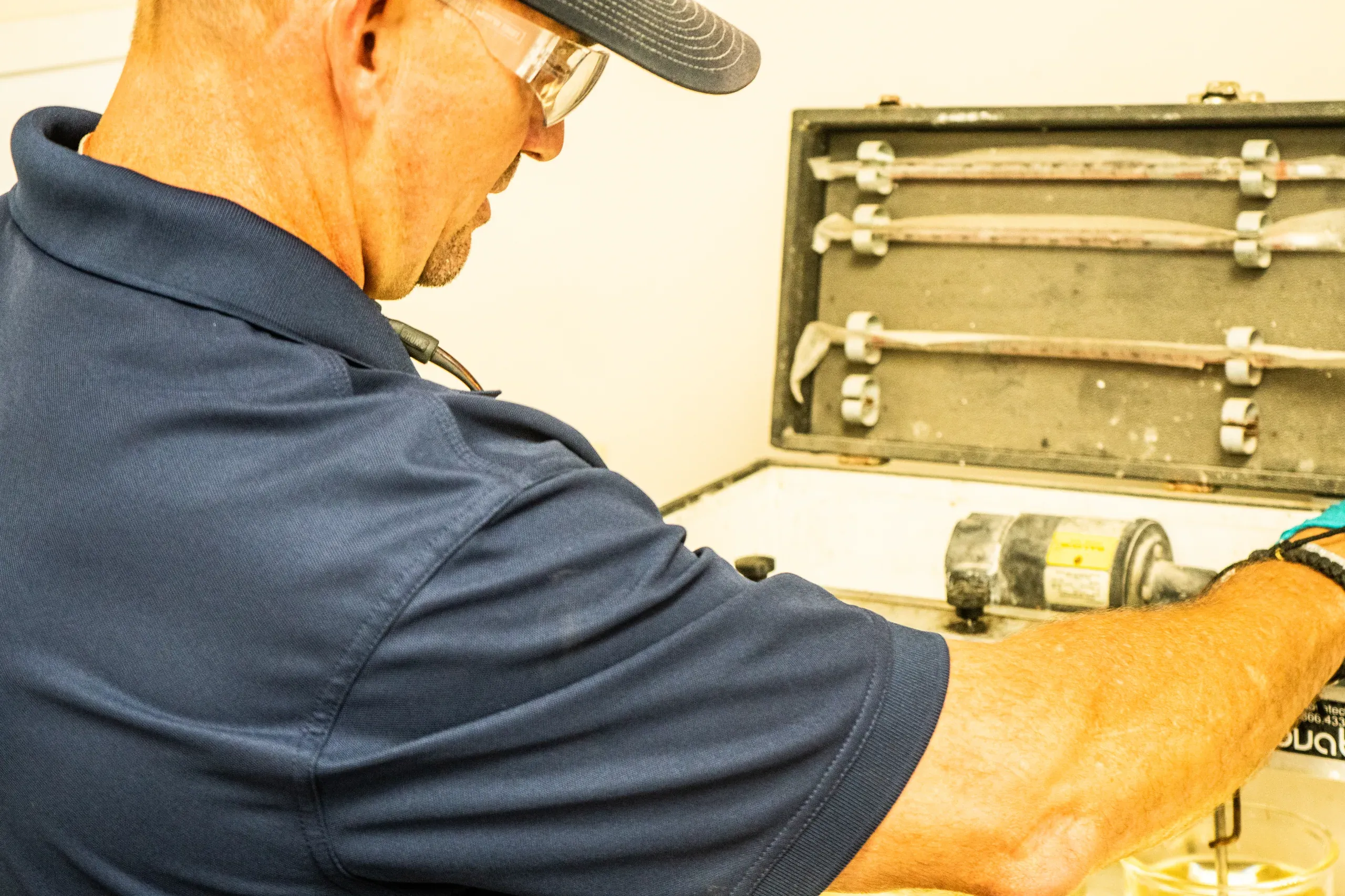 Technician in safety glasses working over an open instrument case at the laboratory bench, running a bench-scale test