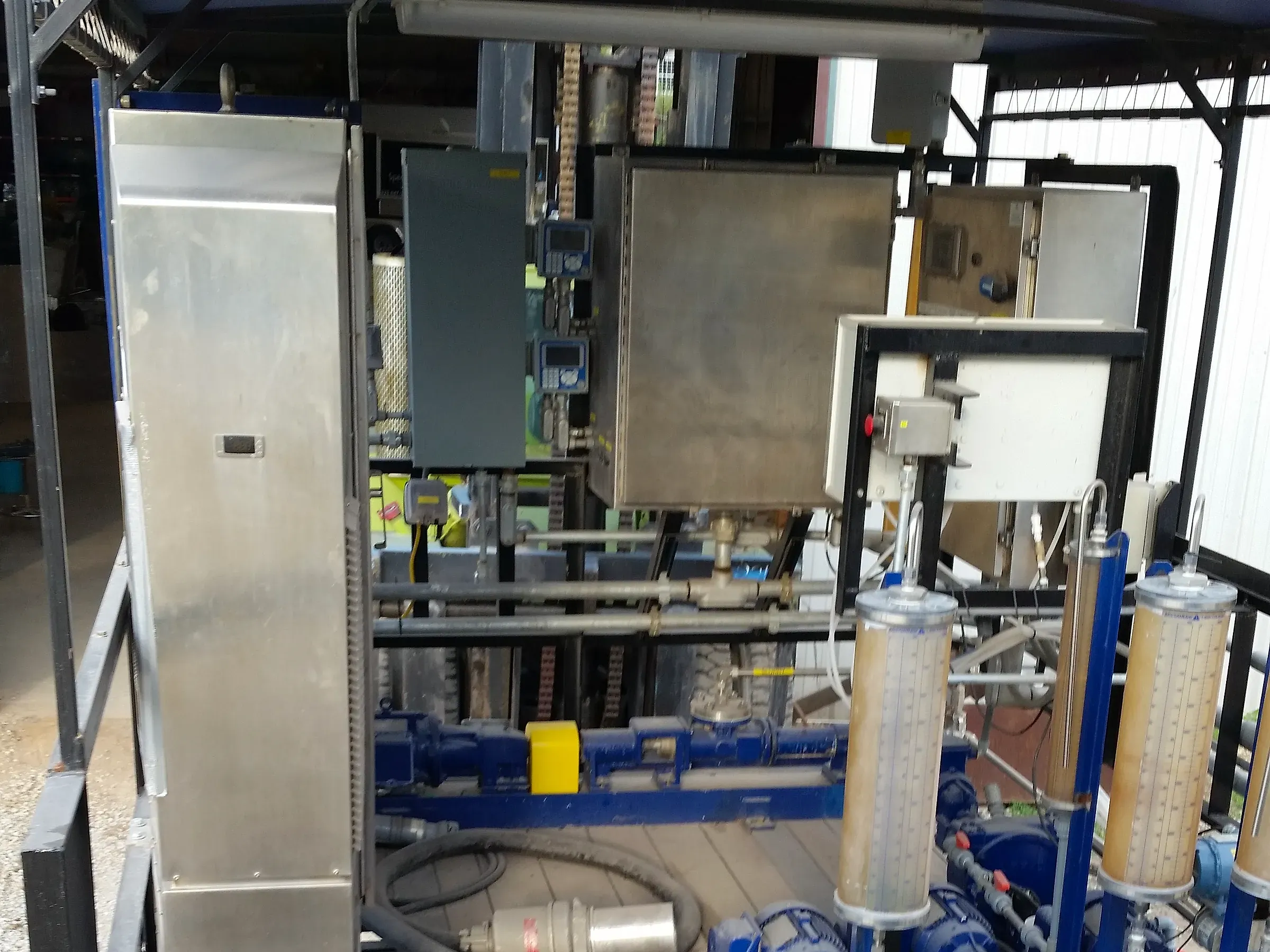 Covered treatment skid with stainless control cabinets, metering pumps and sample lines at a permitted facility