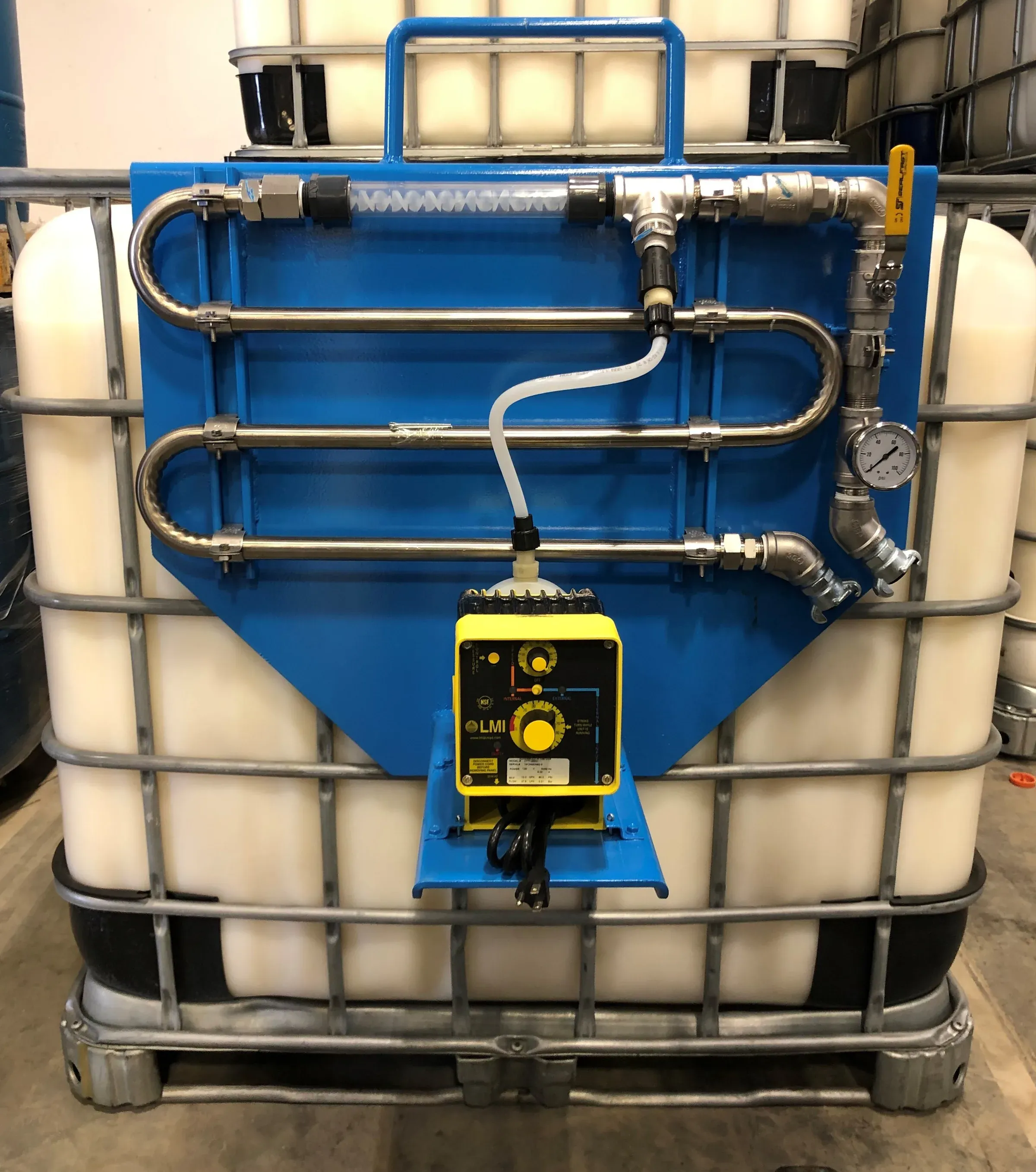 Blue polymer feed panel with stainless injection loop, pressure gauge and LMI metering pump mounted to a white IBC tote in a warehouse