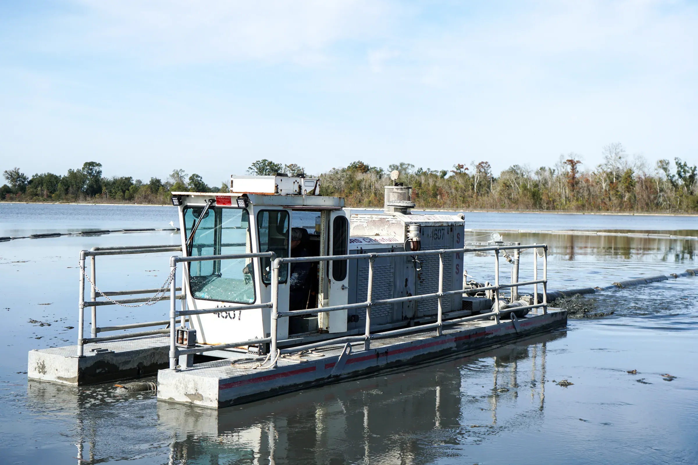 Pontoon dredge working a wide settling lagoon in bright winter light, treeline on the far bank