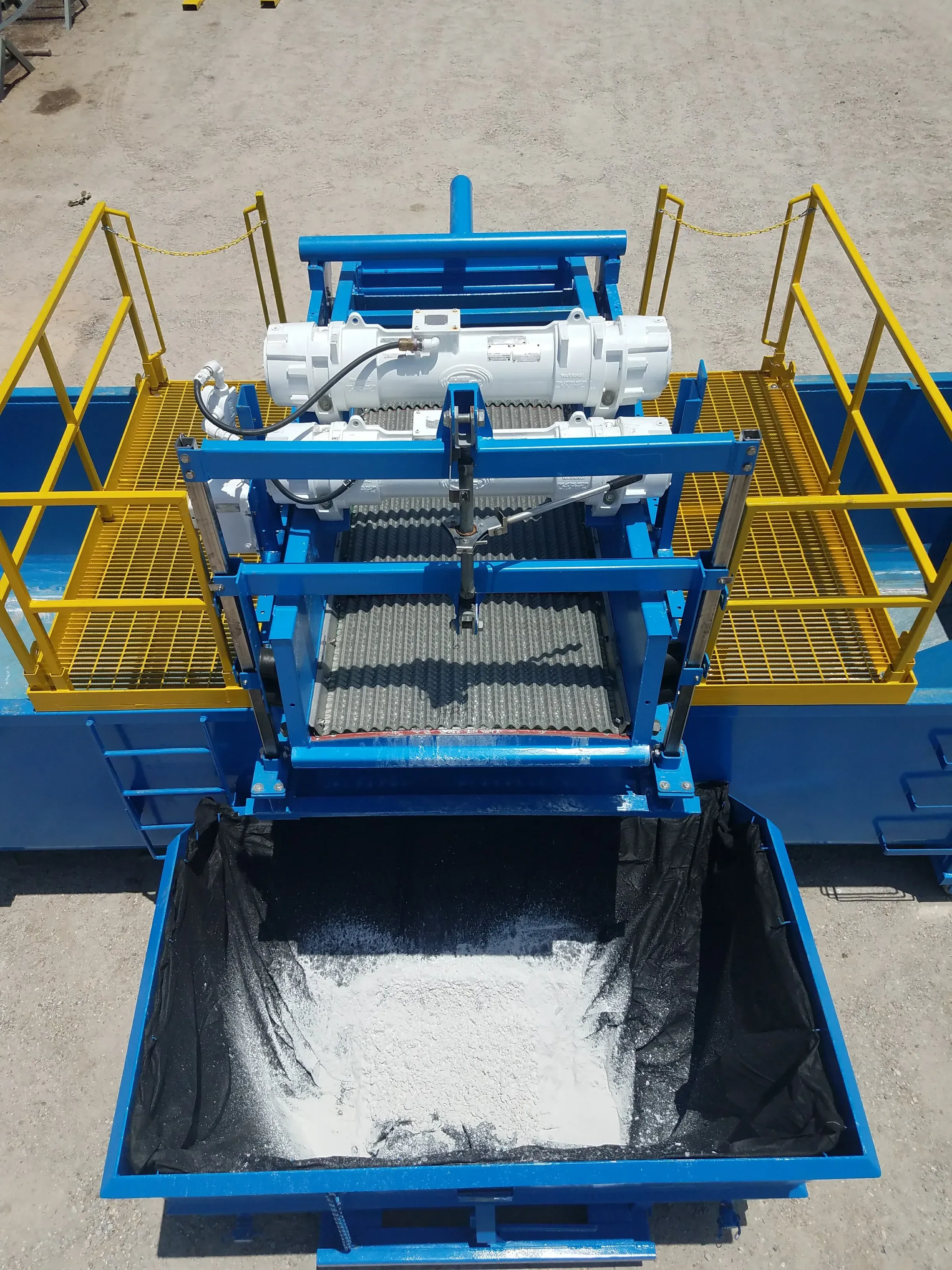 Overhead view of a vibrating shaker screen deck discharging dewatered solids into a lined collection box