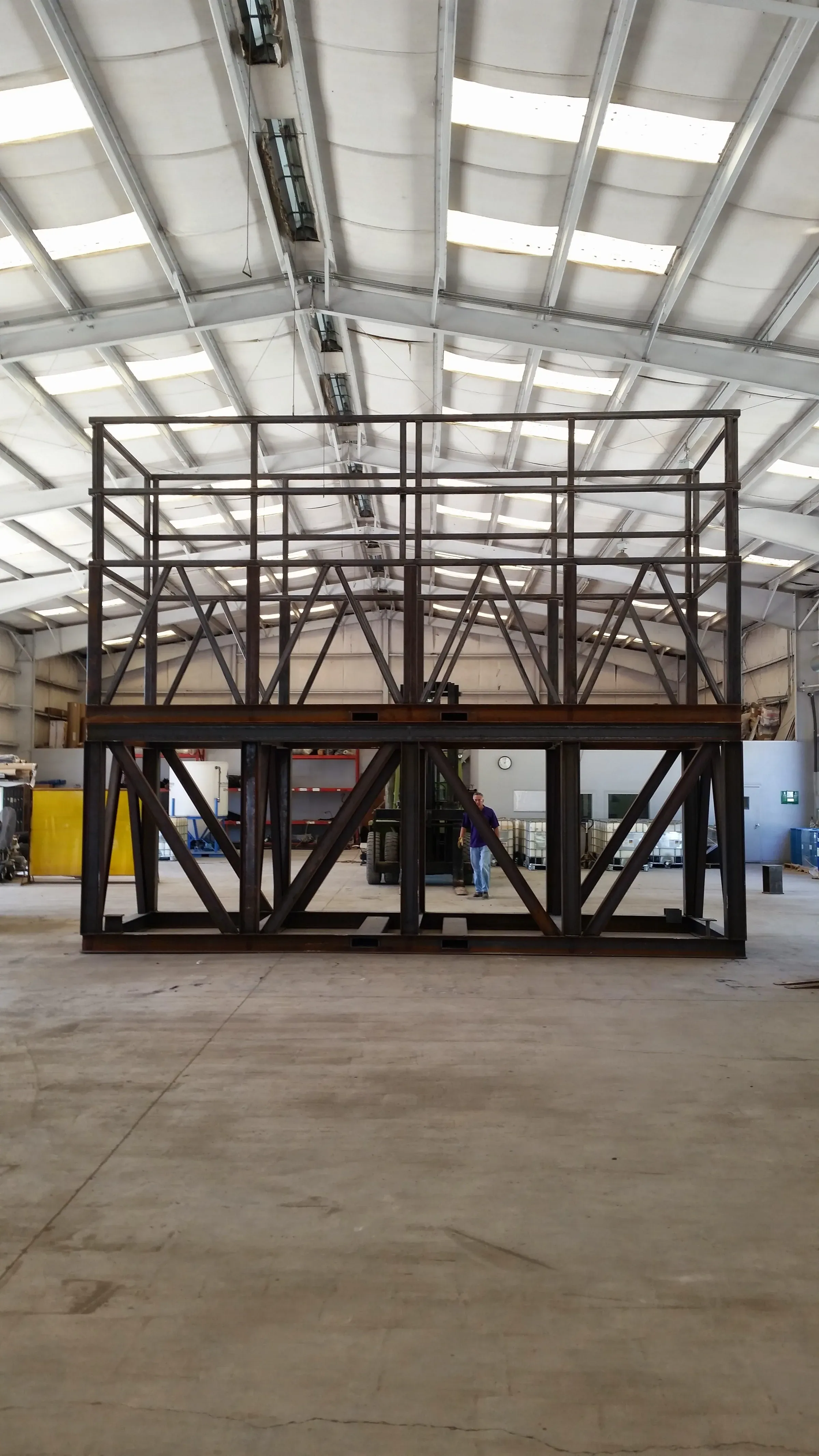 Large two-level structural steel platform frame squared up on the shop floor, a worker standing beneath it for scale