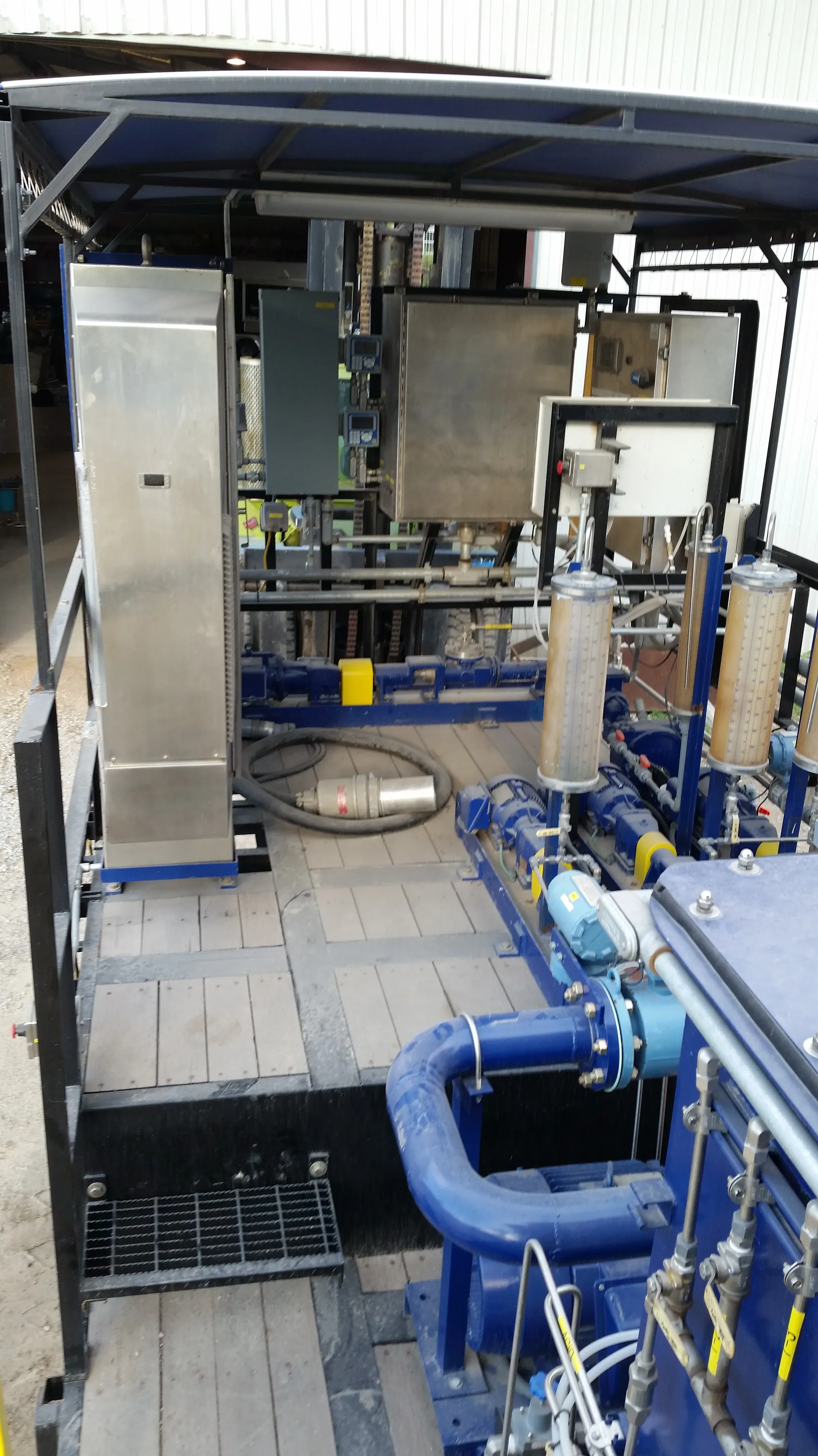 Covered treatment skid with stainless control cabinets, progressive cavity pumps, polymer flow columns and blue suction piping