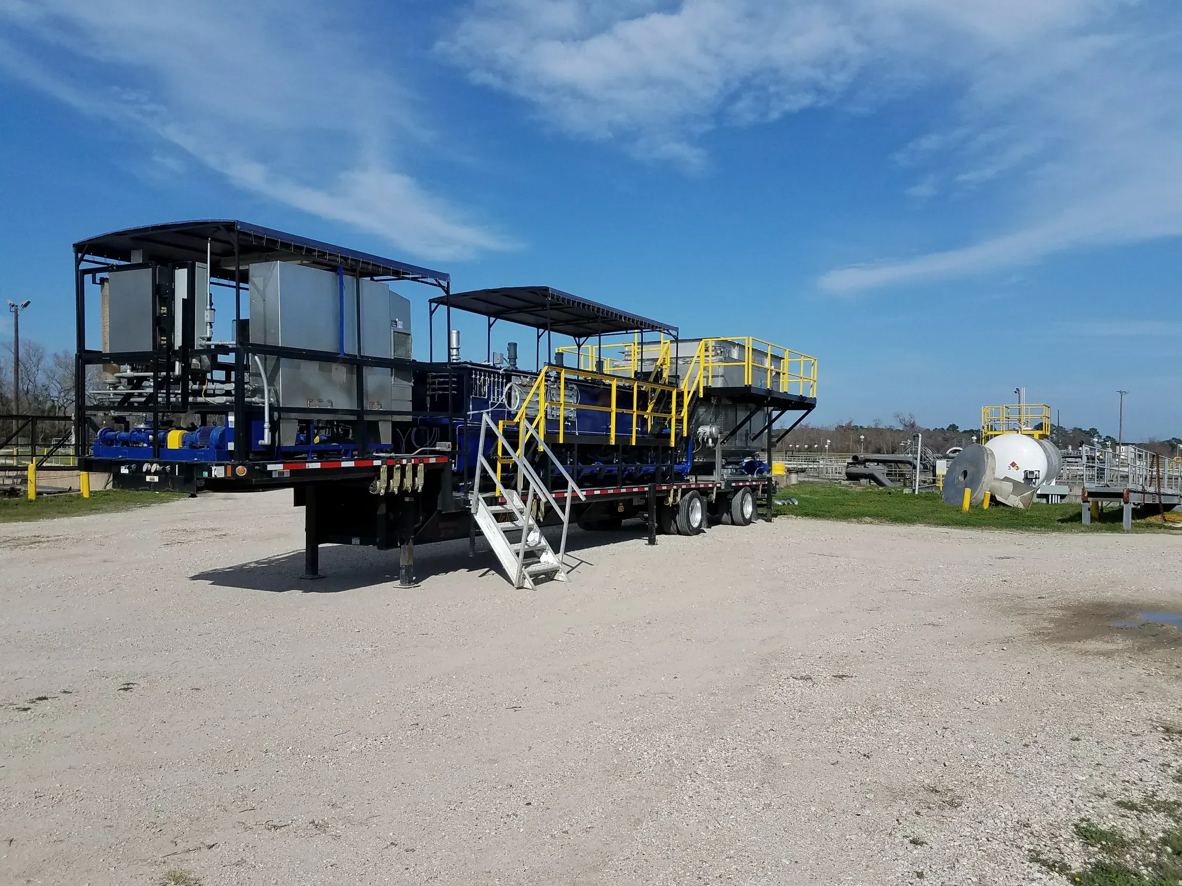 Two trailer-mounted treatment skids with access stairs and yellow handrails staged on gravel at a plant site